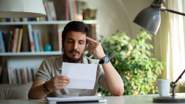 Portrait of a man staring at medical paperwork in frustration. He has his finger on his temple and looks deep in thought.