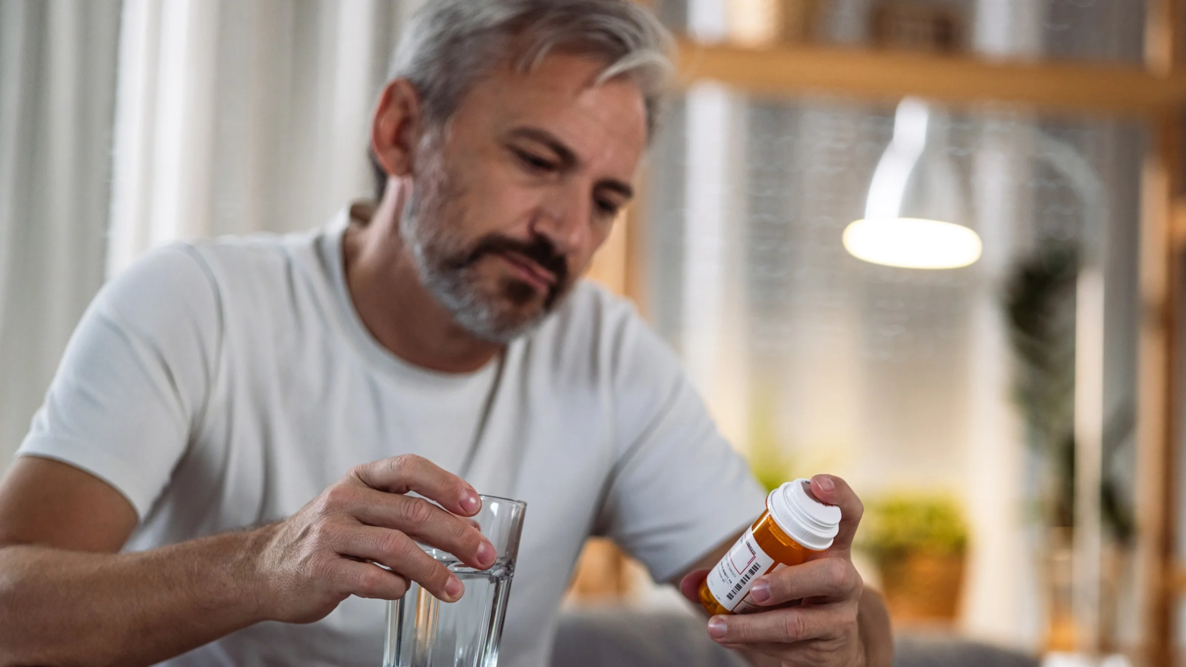 A man reads a prescription bottle at home.