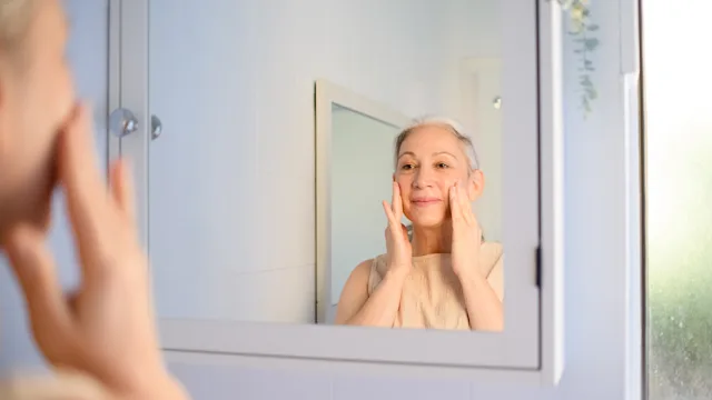 dermatology: senior woman applying face cream 2093434917