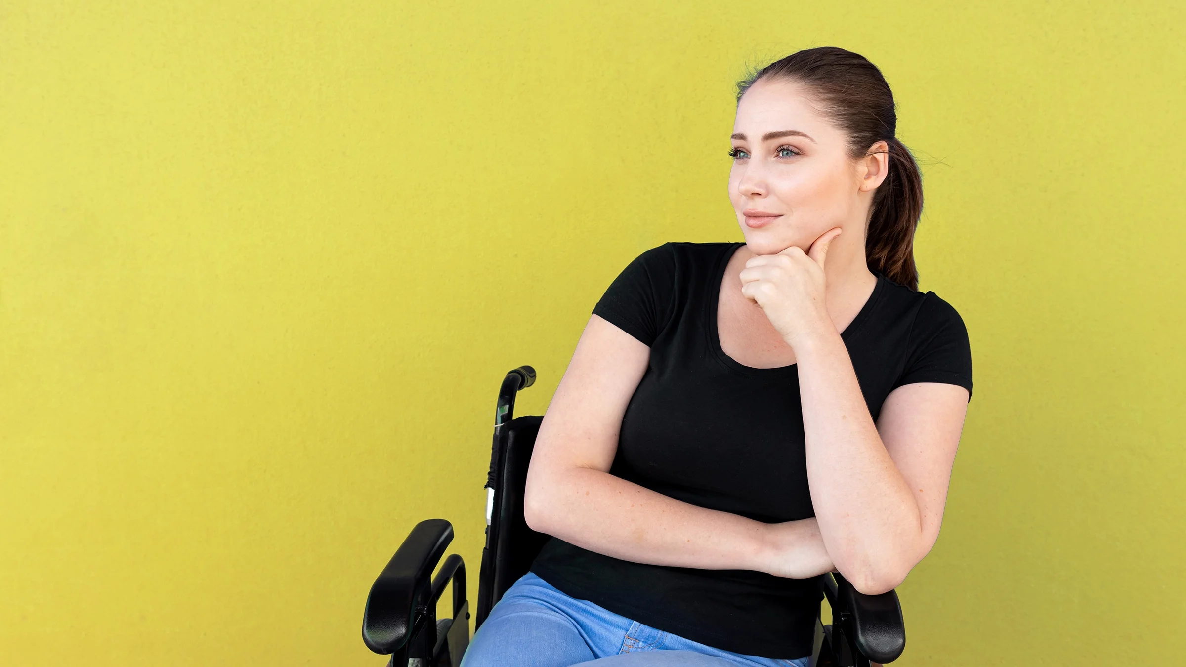 Woman in a wheelchair looking contemplative. She is on a plain yellow studio background.