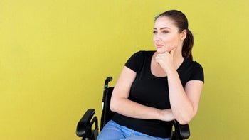 mental-health: young woman in wheelchair looking contemplative-1180324053