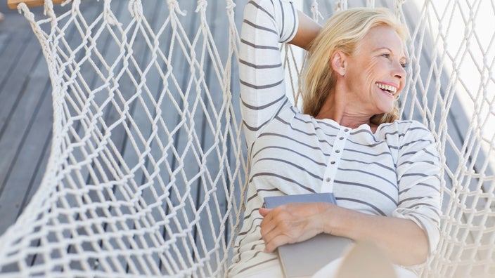 A person relaxing on a hammock and holding a book, letting their eyes rest from reading.