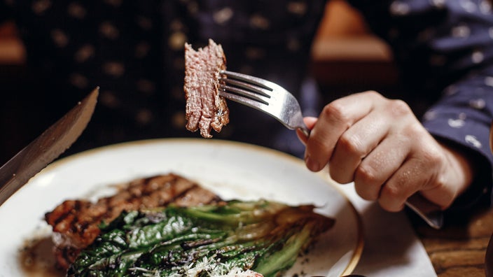 A close-up image shows a person eating a steak.