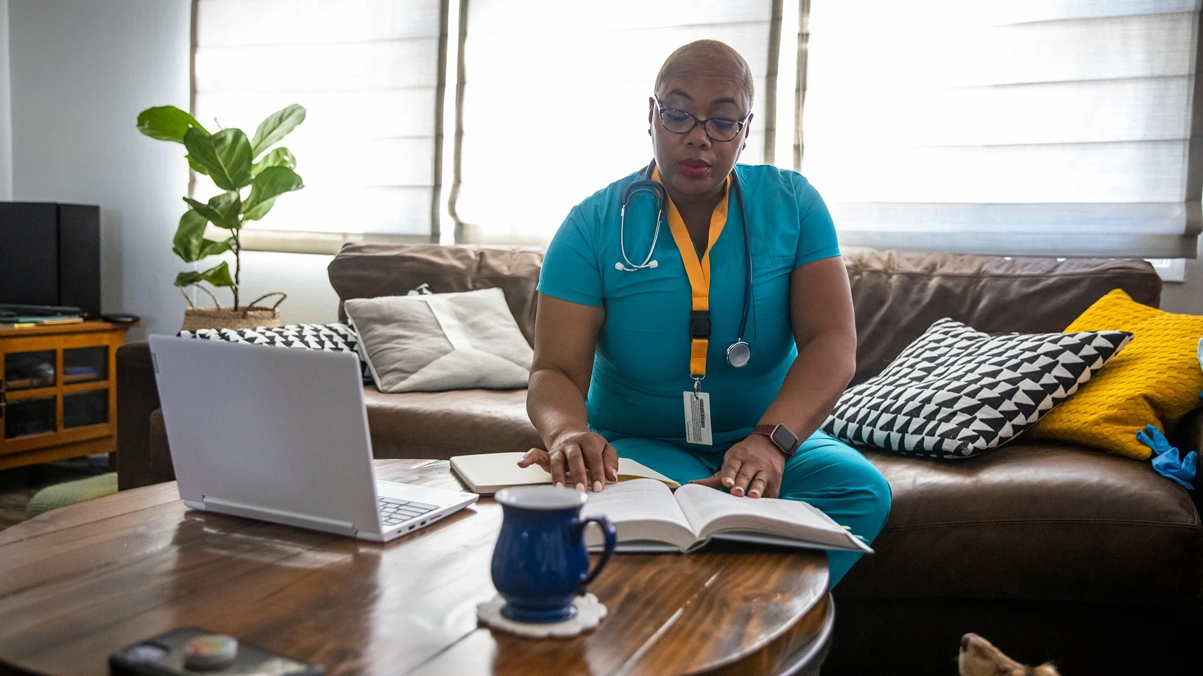 Nurse studying a textbook at home. She is still in her scrubs from work.
