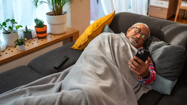 COVID-19: man under a blanket reading smartphone 2079899042