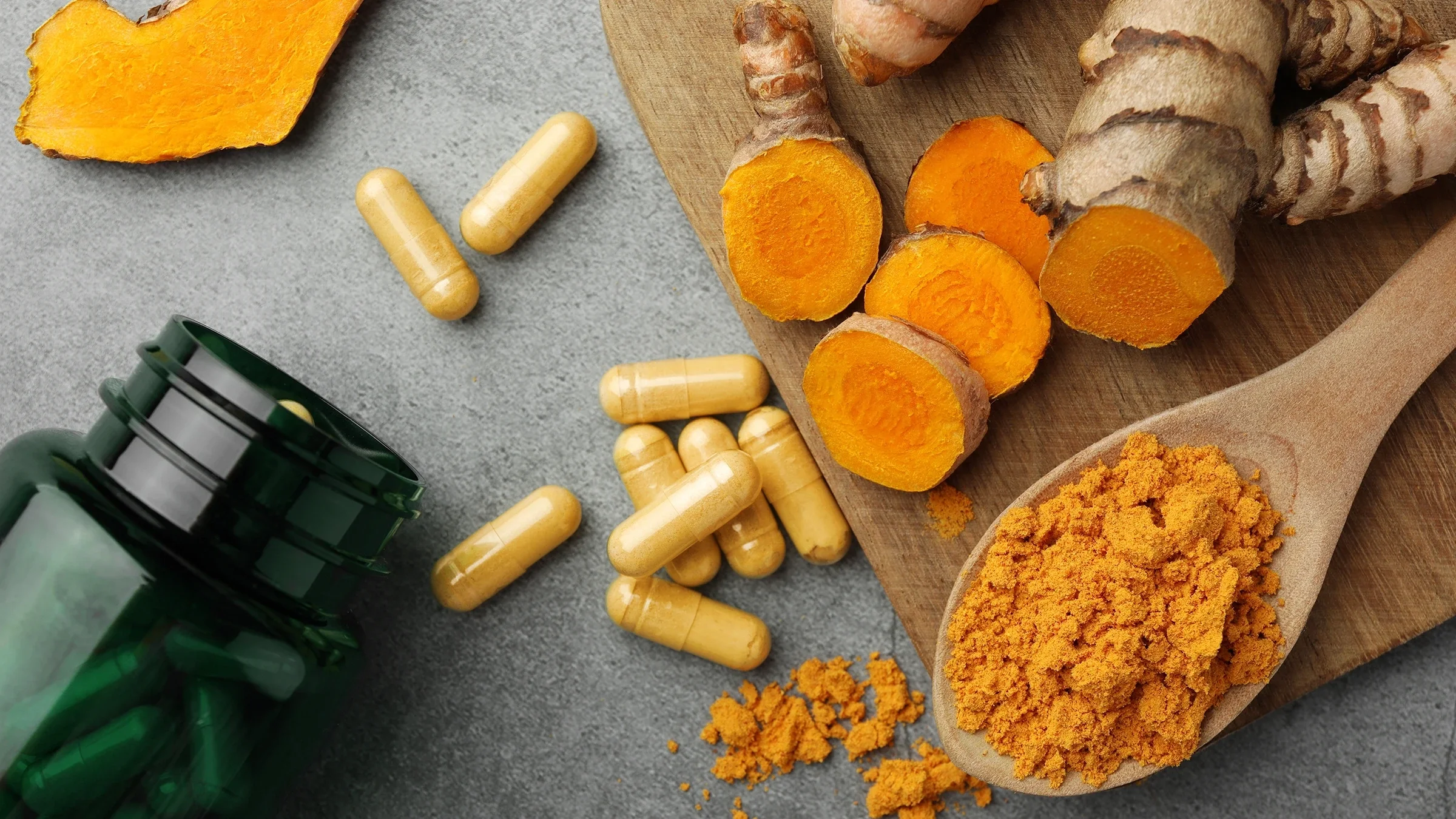 Turmeric powder, pills, and raw turmeric on a table.