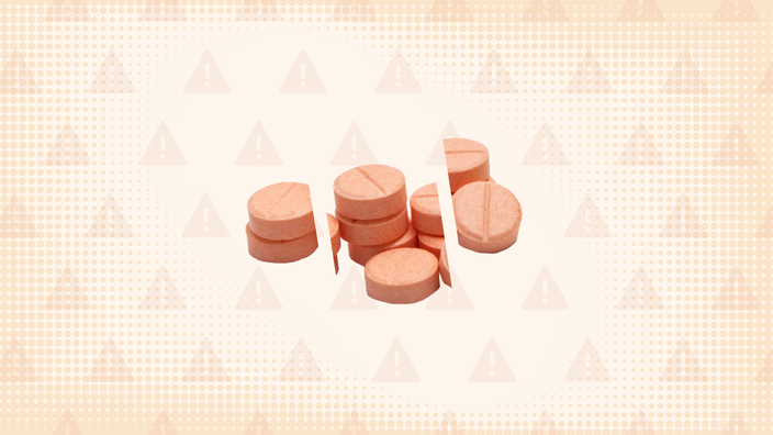 In the center of an orange background with texture and warning sign pattern is a pile of chalky orange pills cut into thirds. 