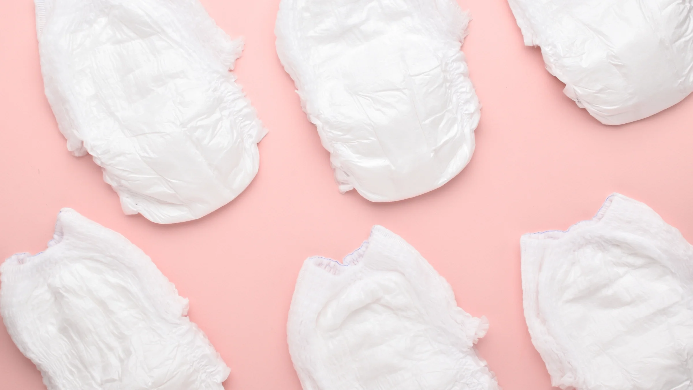 Six white diapers creating a pattern on a light-pink background.
