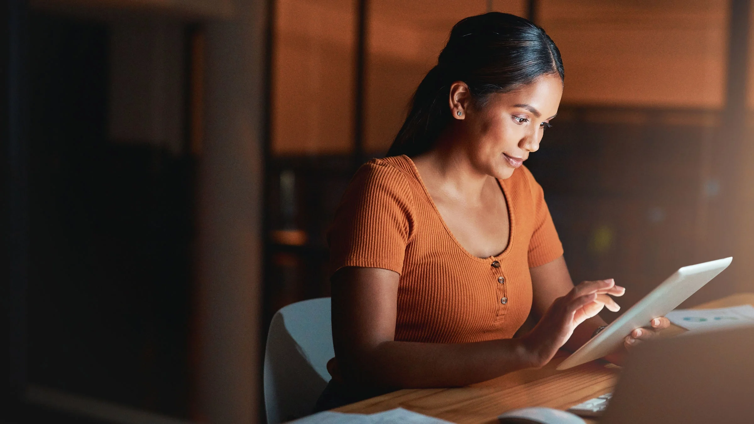 A woman sits in a dark room looking at a tablet.
