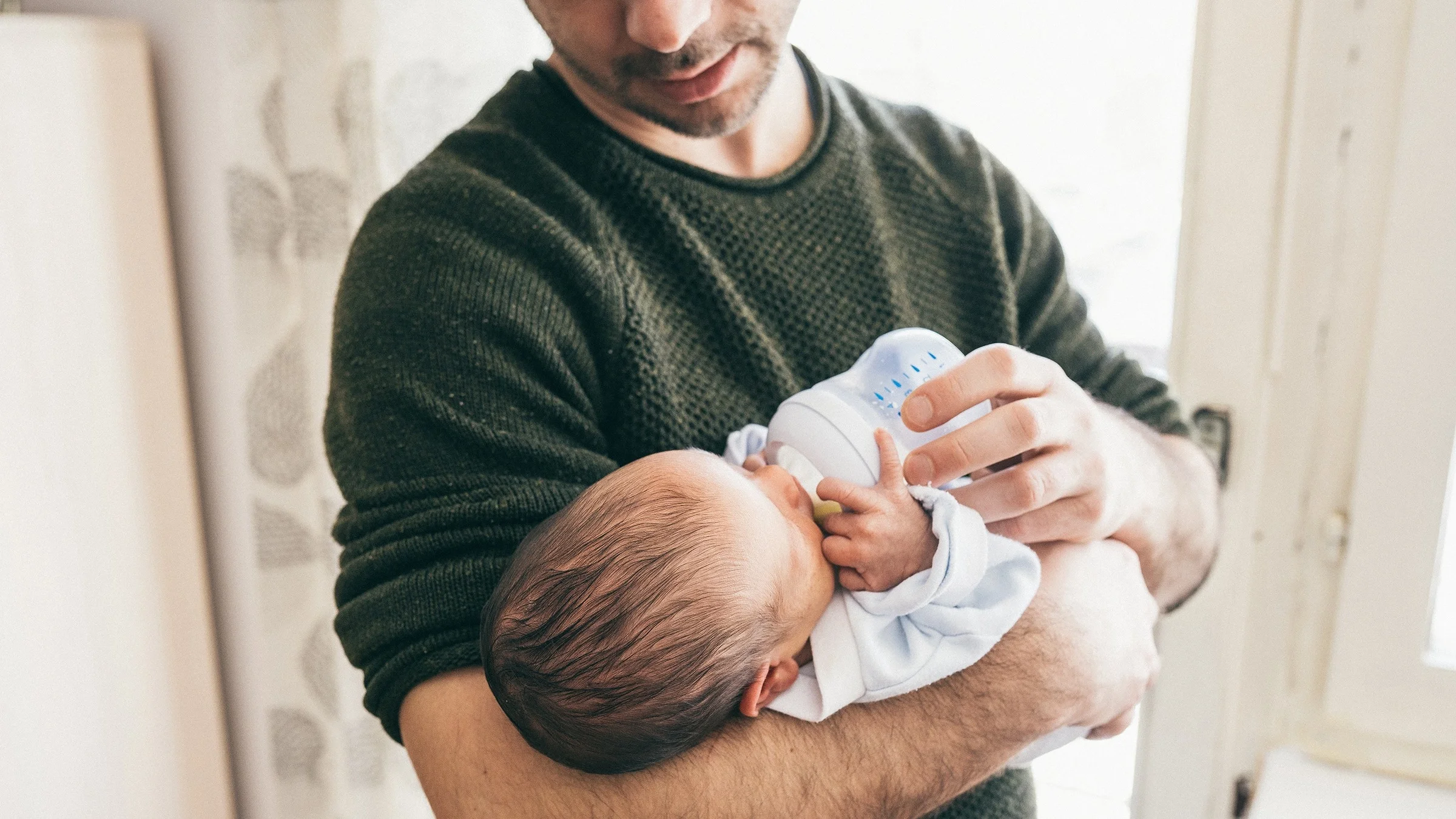 Young father holding his newborn and feeding them a bottle.