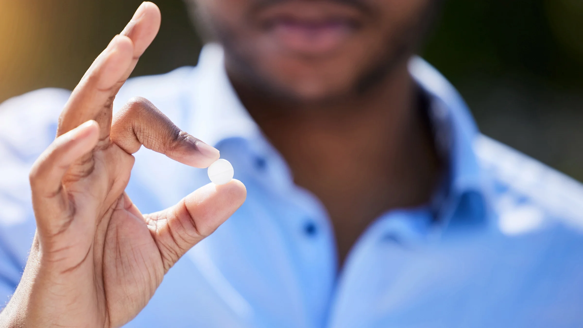 A man holds one single pill between his thumb and forefinger.