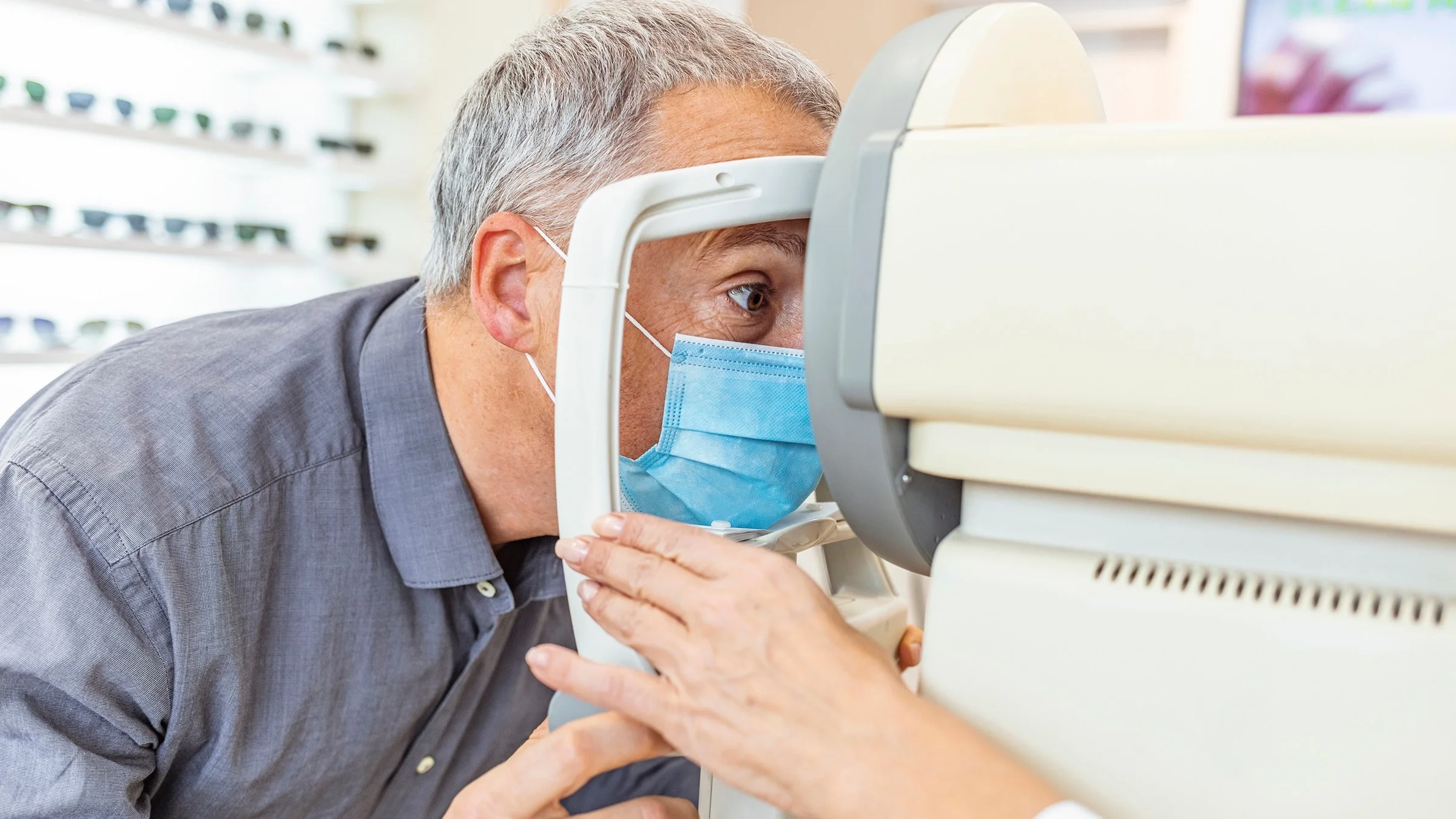 Close-up of a man at the eye doctors office. He is looking into the test machine while the doctors adjusts the head rest.