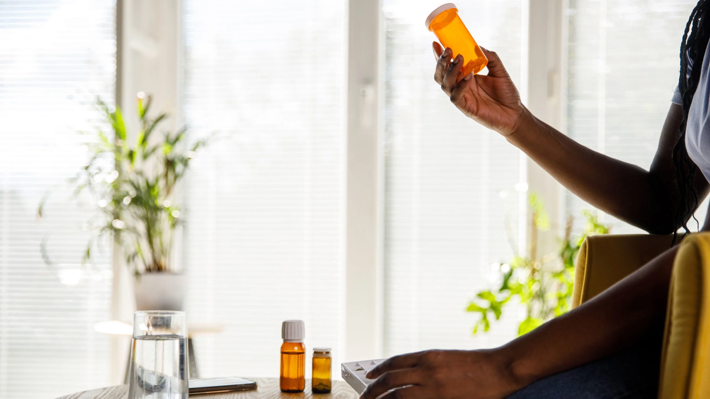 Woman sitting at her coffee table, holding a pill box and reading the label.