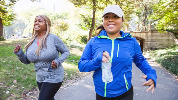 Two women run outdoors through a park.