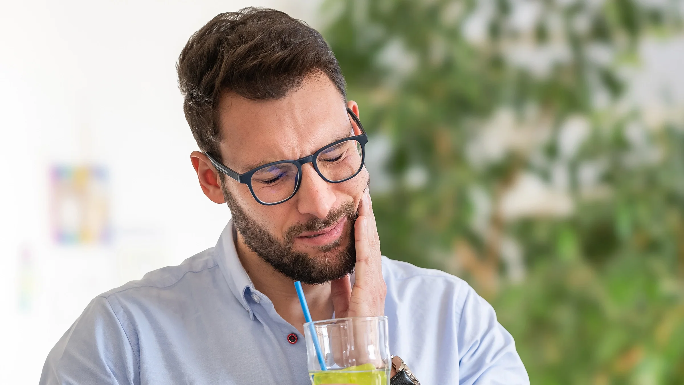 Man in pain touching his jaw while holding a drink with a straw.