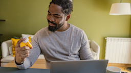 Man holding prescription bottle as he reviews information online on his laptop.
blackCAT/E+ via Getty Images