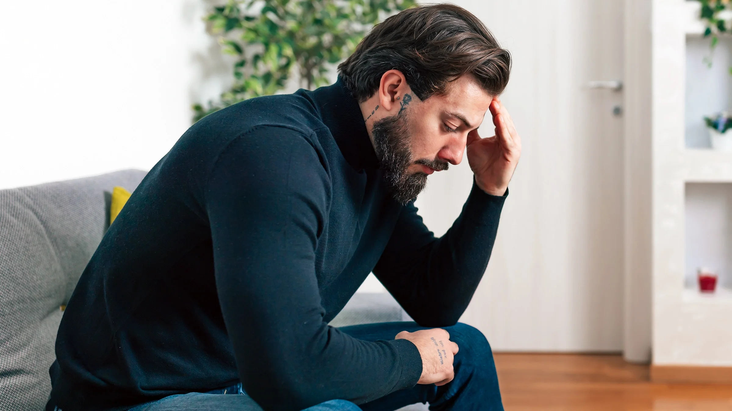 Man sitting in his living room with a depressed look on his face and holding his head