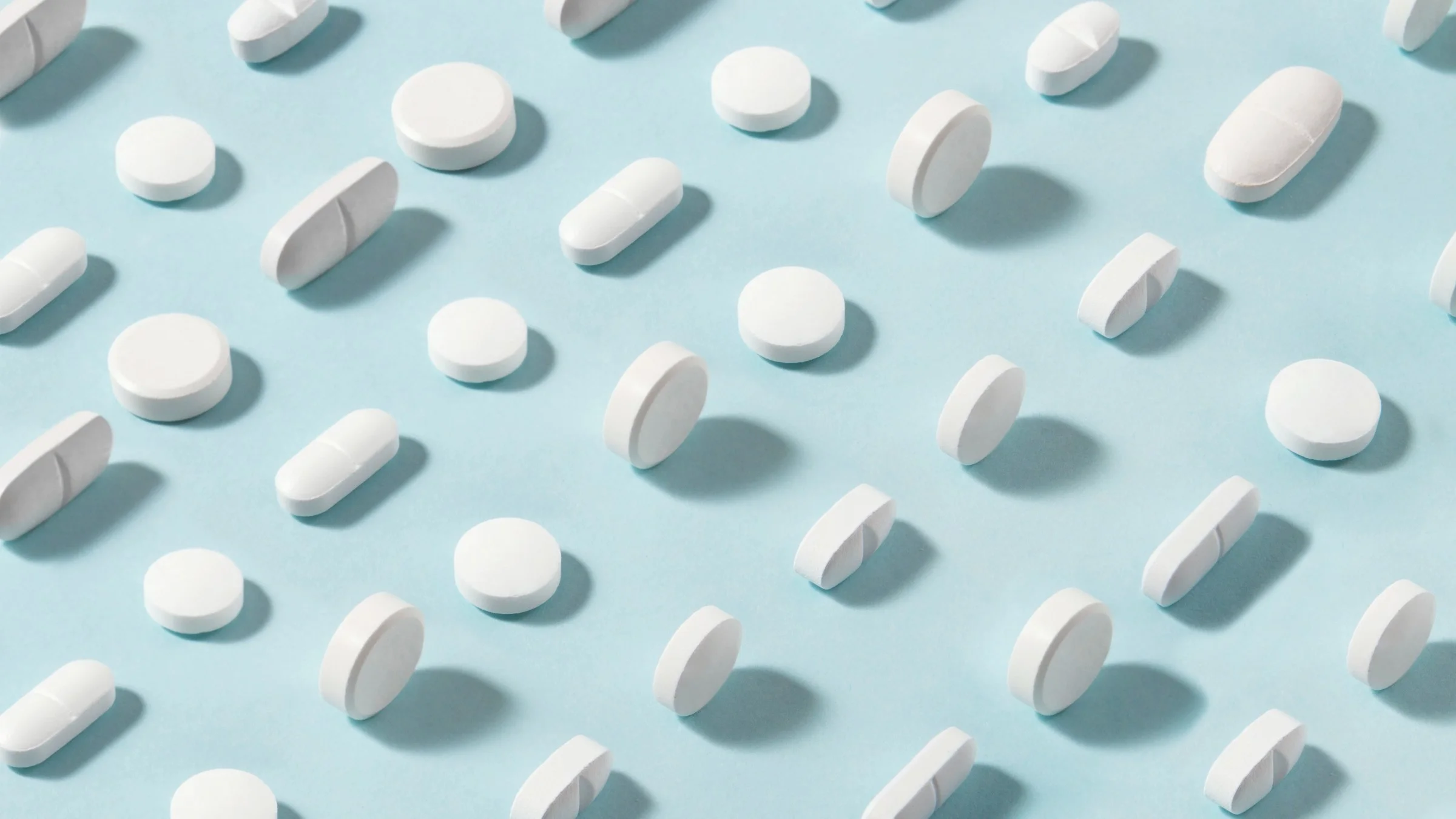 Patter of two types of white pills on a light blue background.