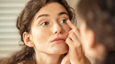 Close-up of a woman putting in a contact lens in her eye. The perspective is of her reflection in the mirror.
Ridofranz/iStock via Getty Images