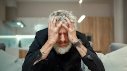 Man sitting on the couch clutching his head.
LanaStock/iStock via Getty Images Plus