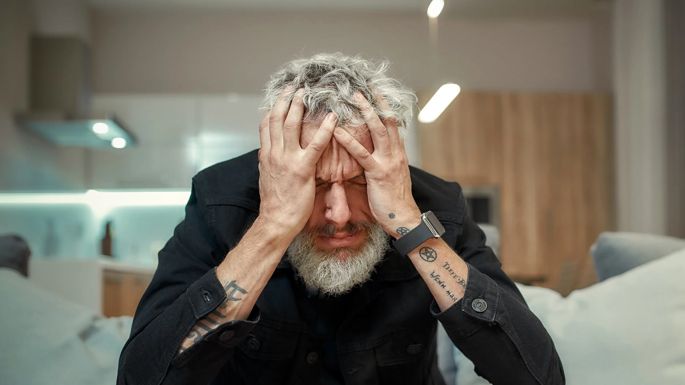 Man sitting on the couch clutching his head.