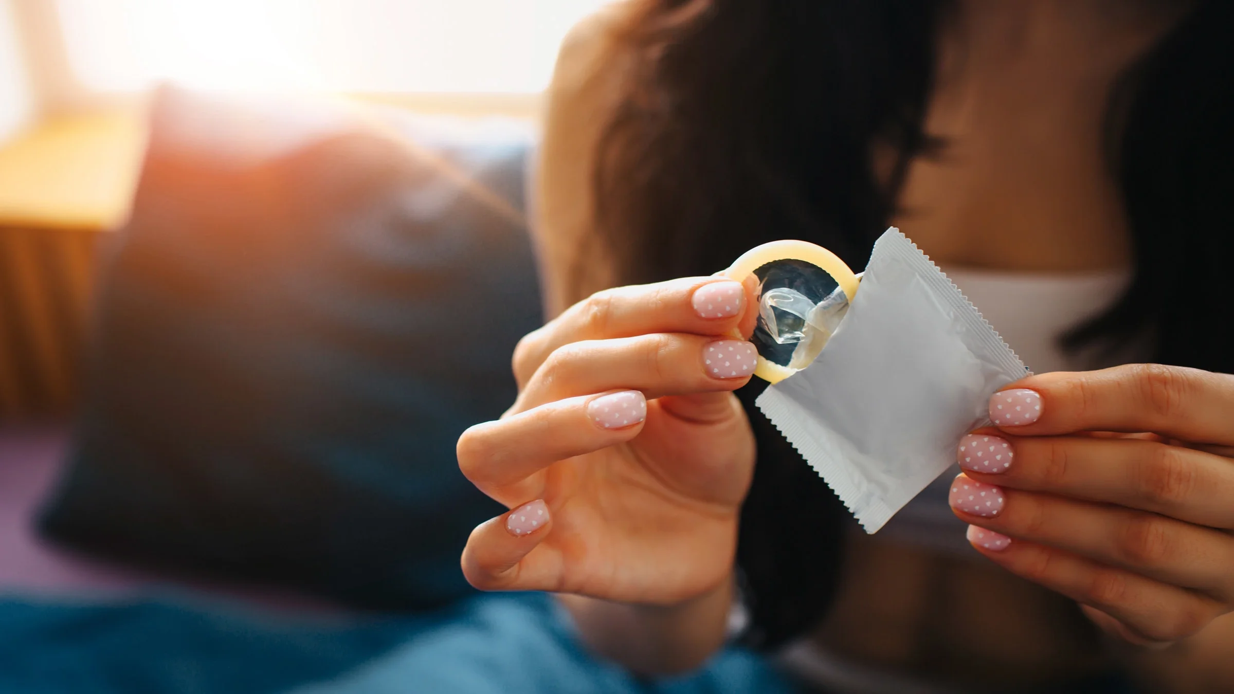 Cropped shot of a person with polka dotted nails unwrapping a condom. 