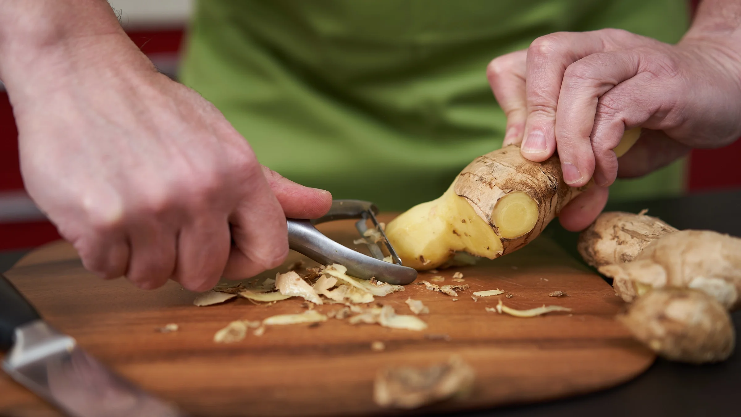A man peels ginger on a wooden board. 