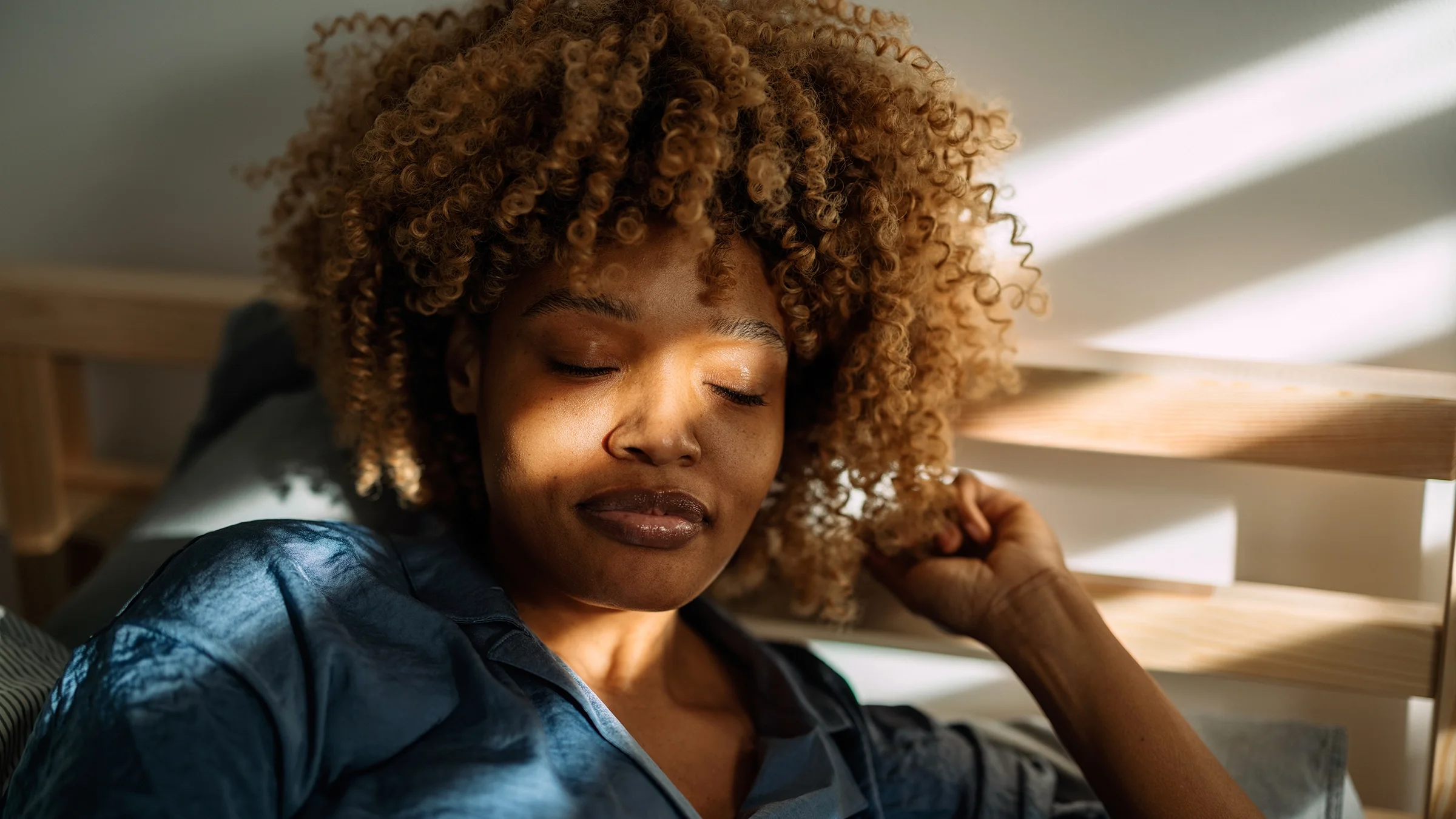 A woman wakes up in the morning with sunlight on her face.