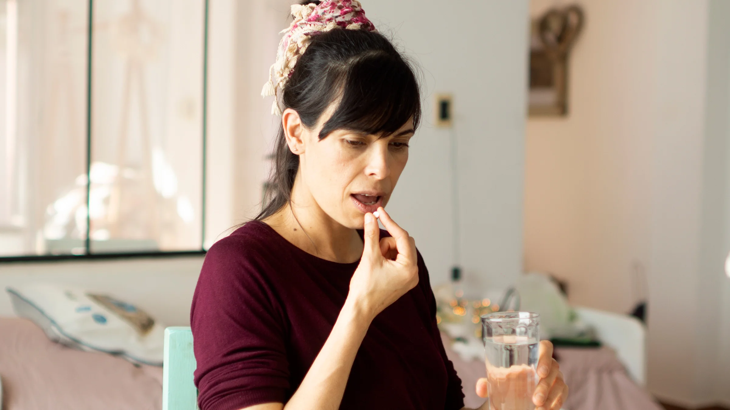 A woman takes medication with a glass of water.