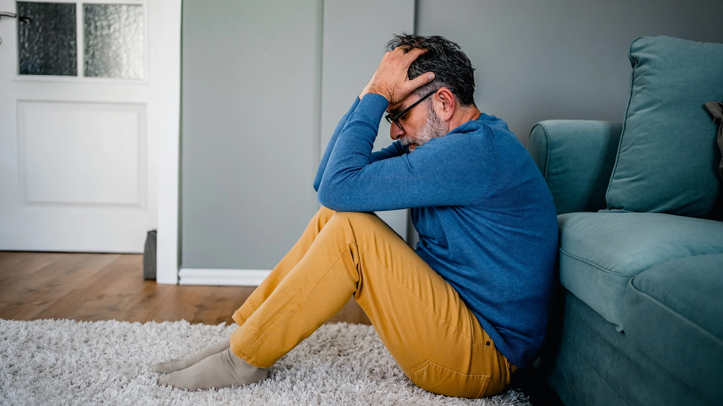 Man sitting alone on the floor at home with face in his hands.