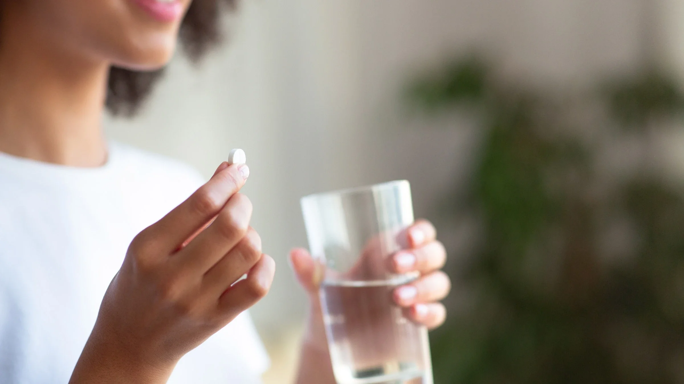 A cropped shot of someone holding a pill and a glass of water.