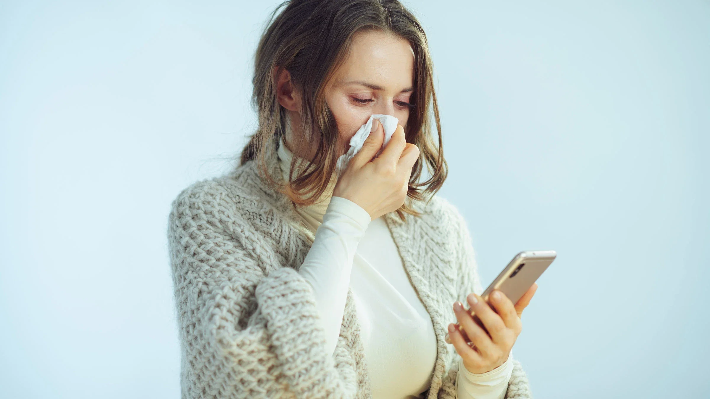 A sick person blowing this nose and searching for remedies on their phone.
CentralITAlliance/iStock via Getty Images Plus 