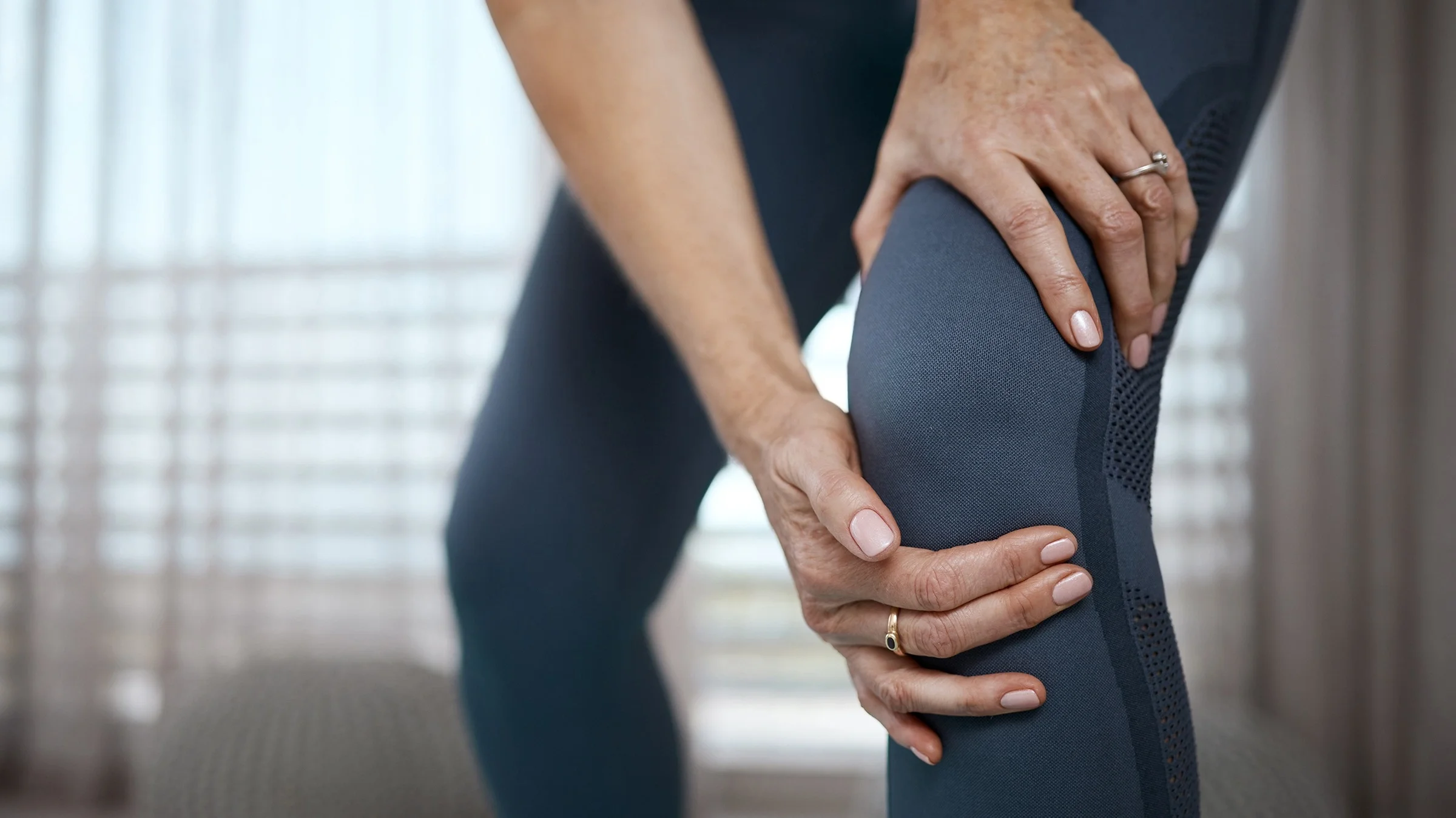 Cropped close-up of a woman grabbing her knee in pain.