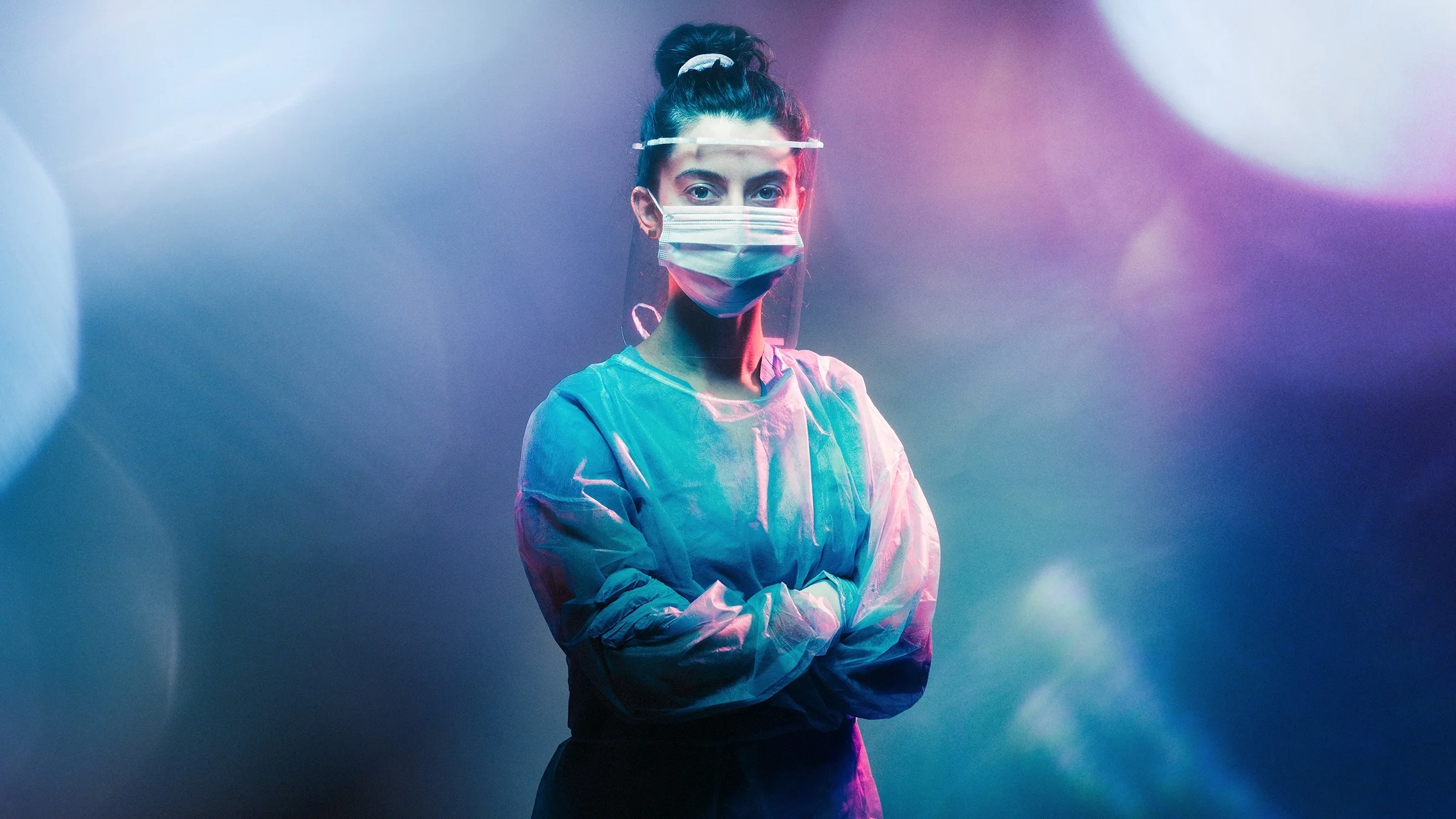 Glossy studio portrait of a nurse with lens flairs and gradient lights shining on them. The background is blue and purple lights.