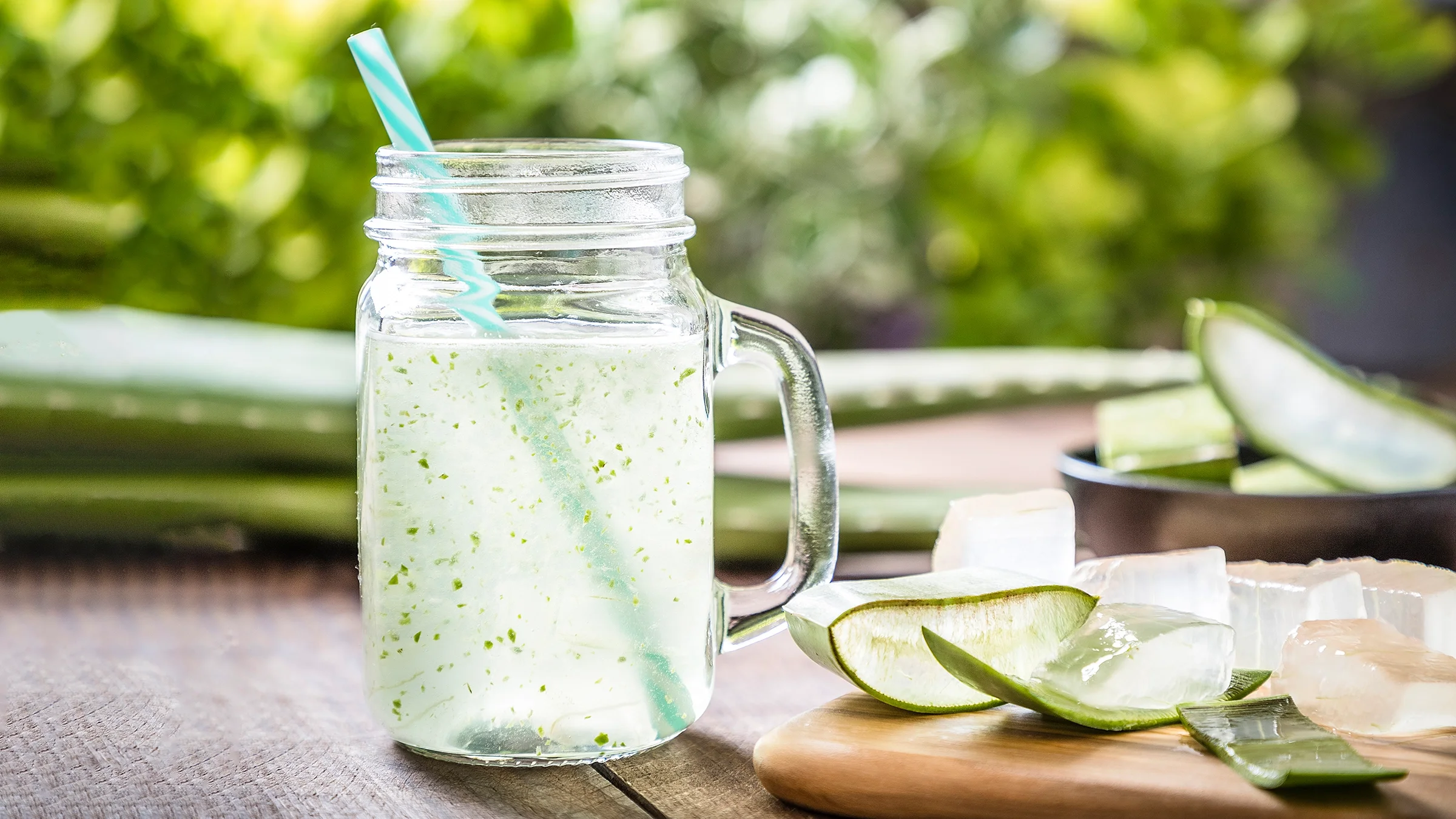 Aloe vera juice in a mason jar with aloe vera pieces on the table next to it.