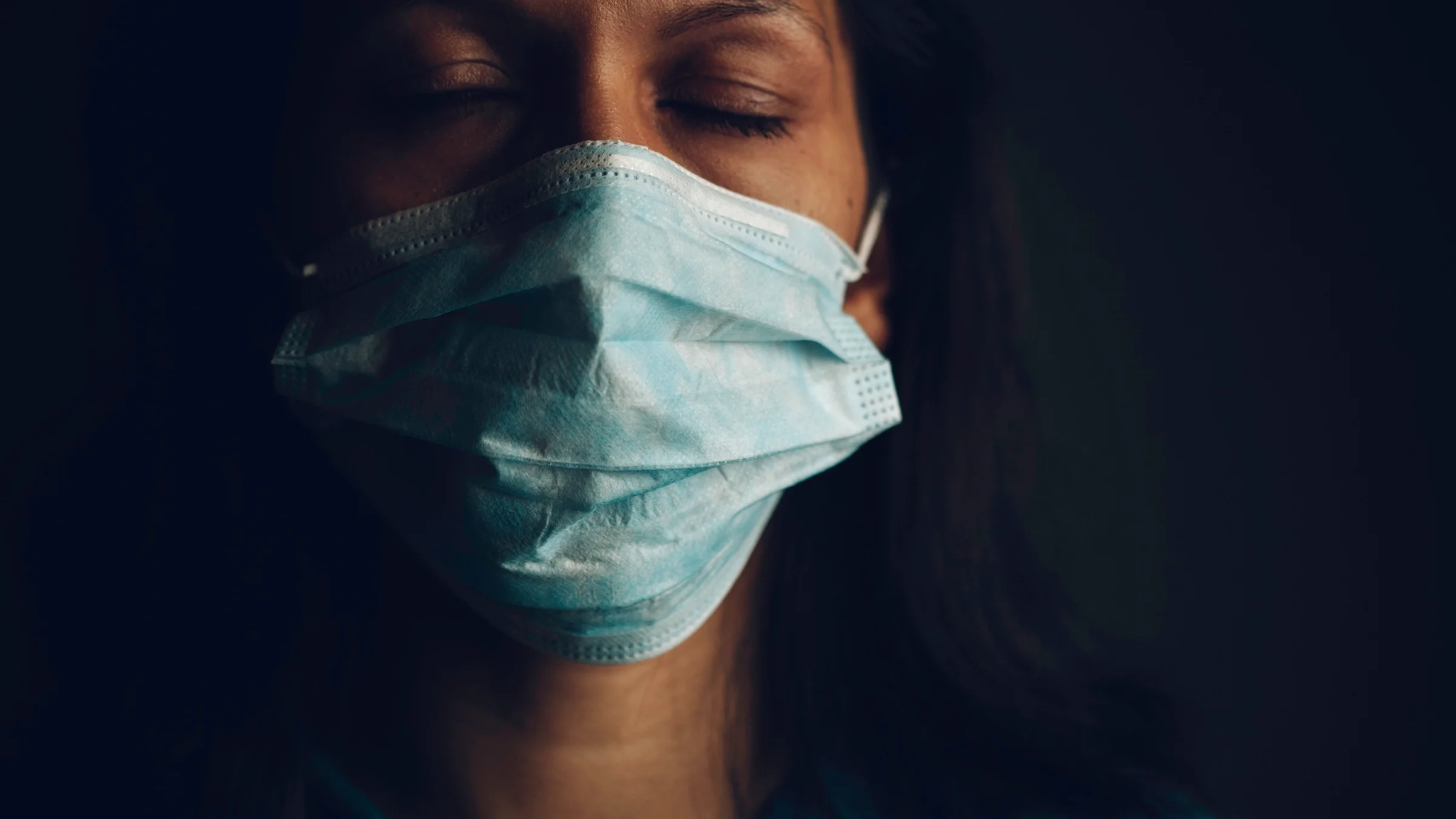 Close-up portrait of a doctor wearing a face mask and closing their eyes.