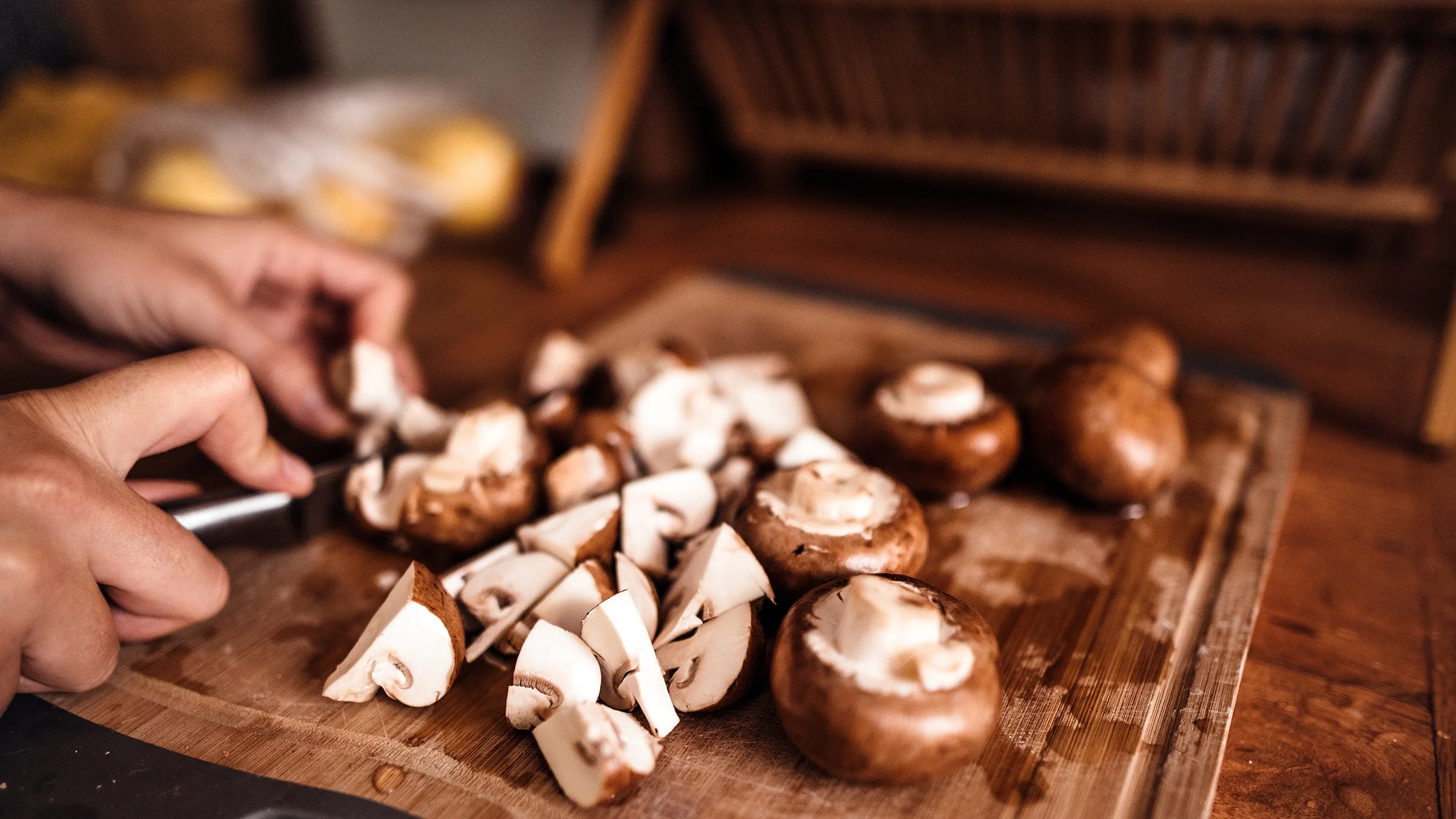A person chops mushrooms on a cutting board. 