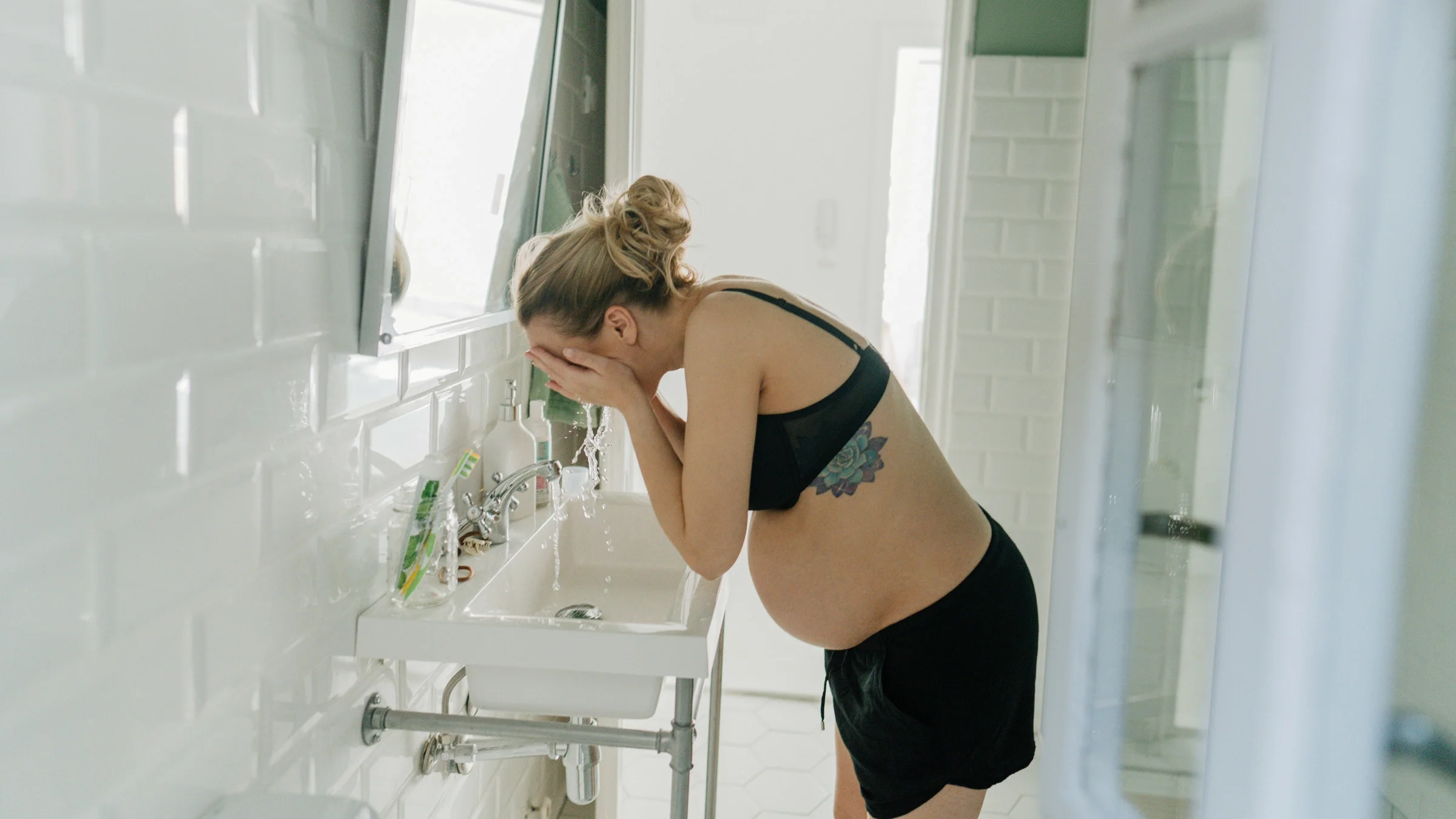 A pregnant person washing their face.