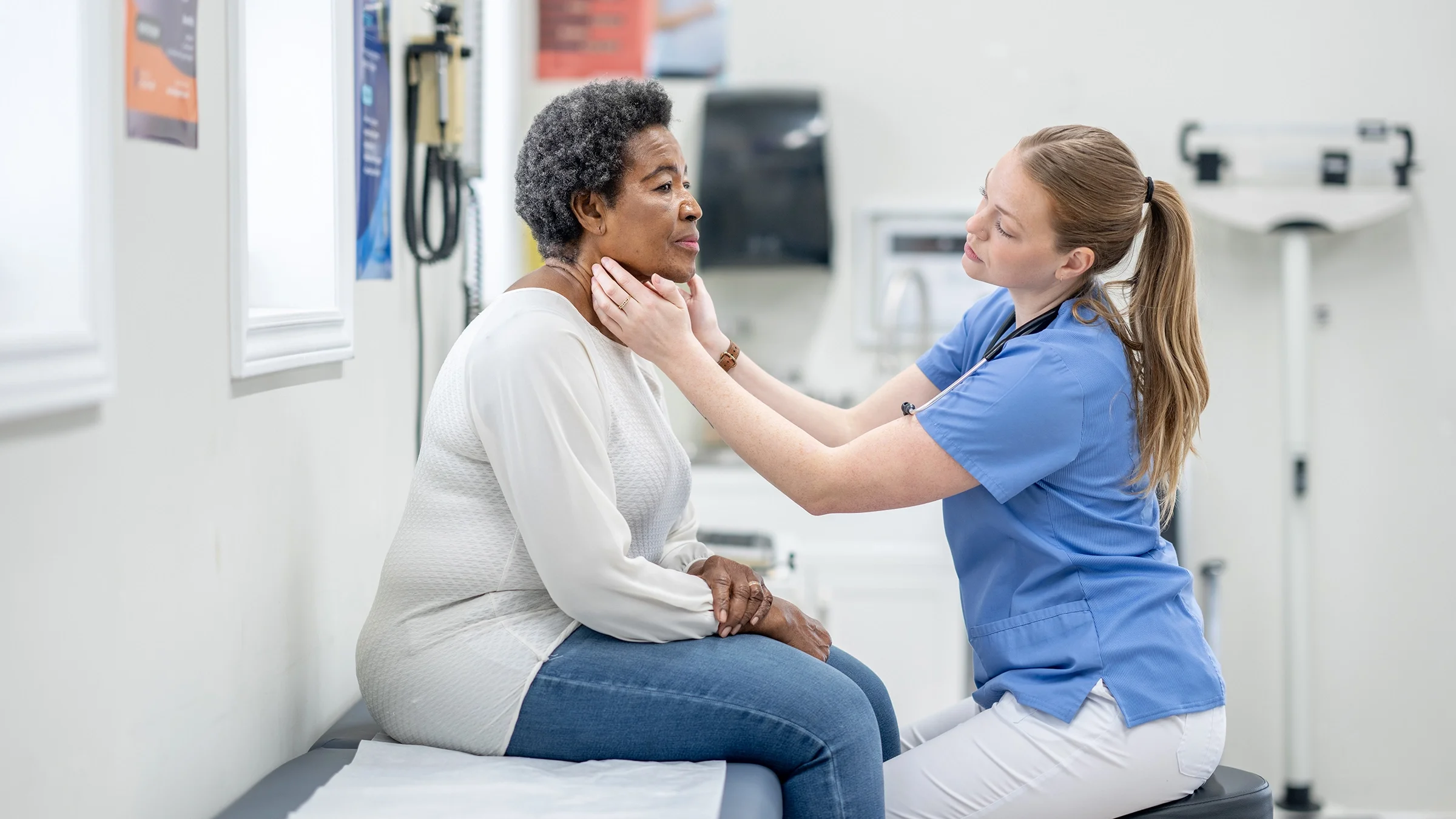 Healthcare professional examining a woman's thyroid.
