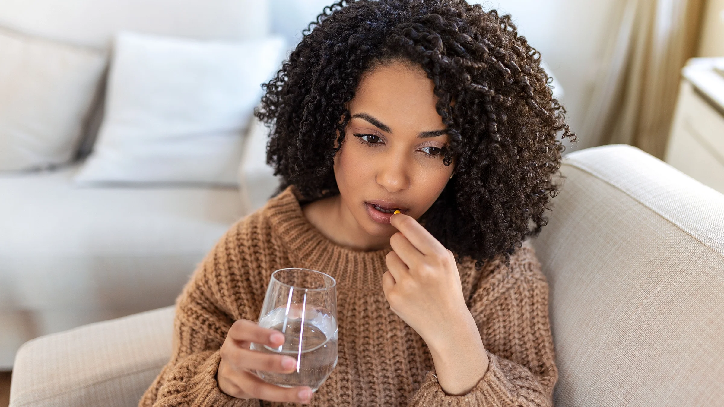 A woman is taking a pill with a glass of water.