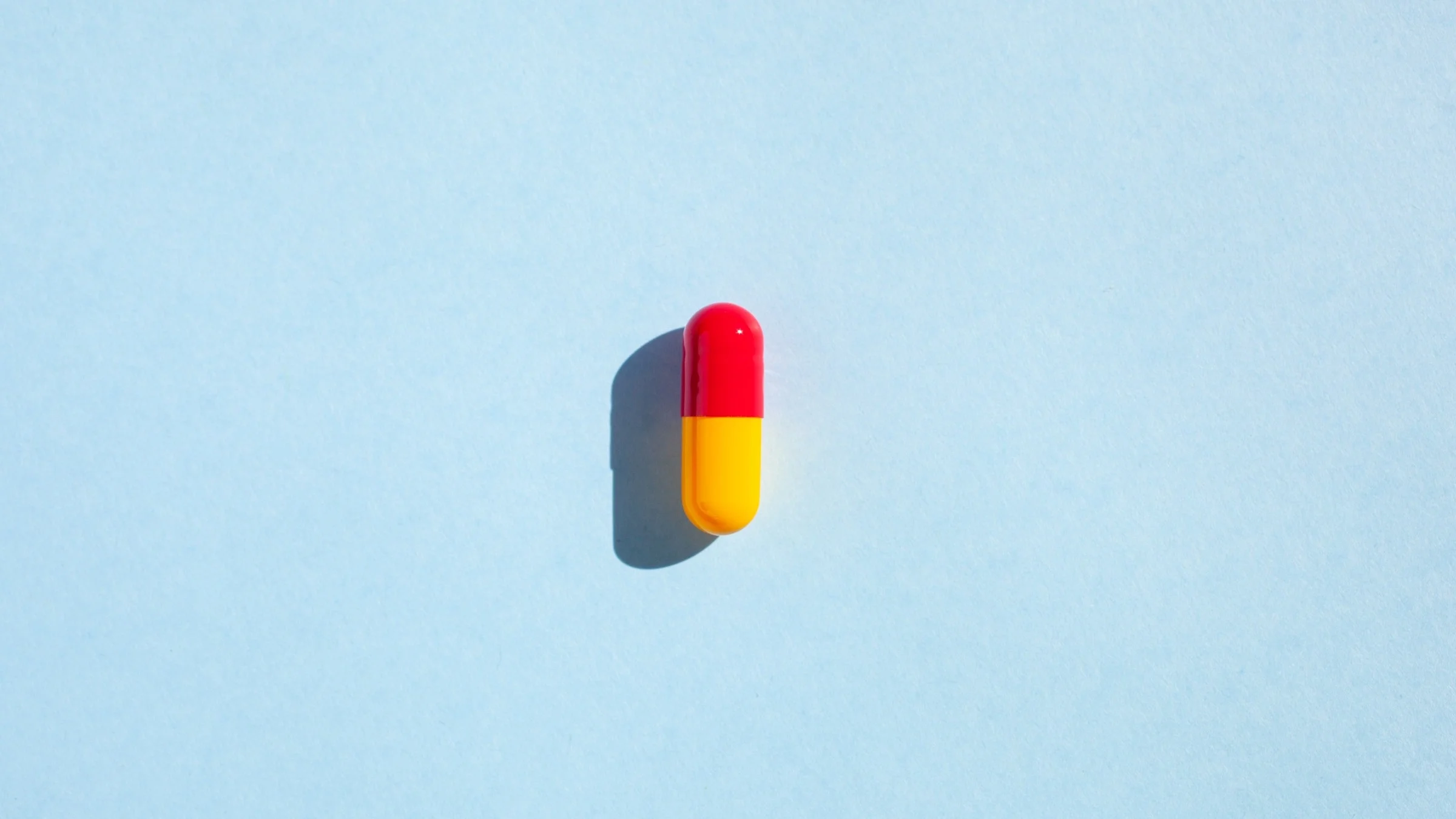 Over head shot of a red and yellow pill capsule on light blue background.