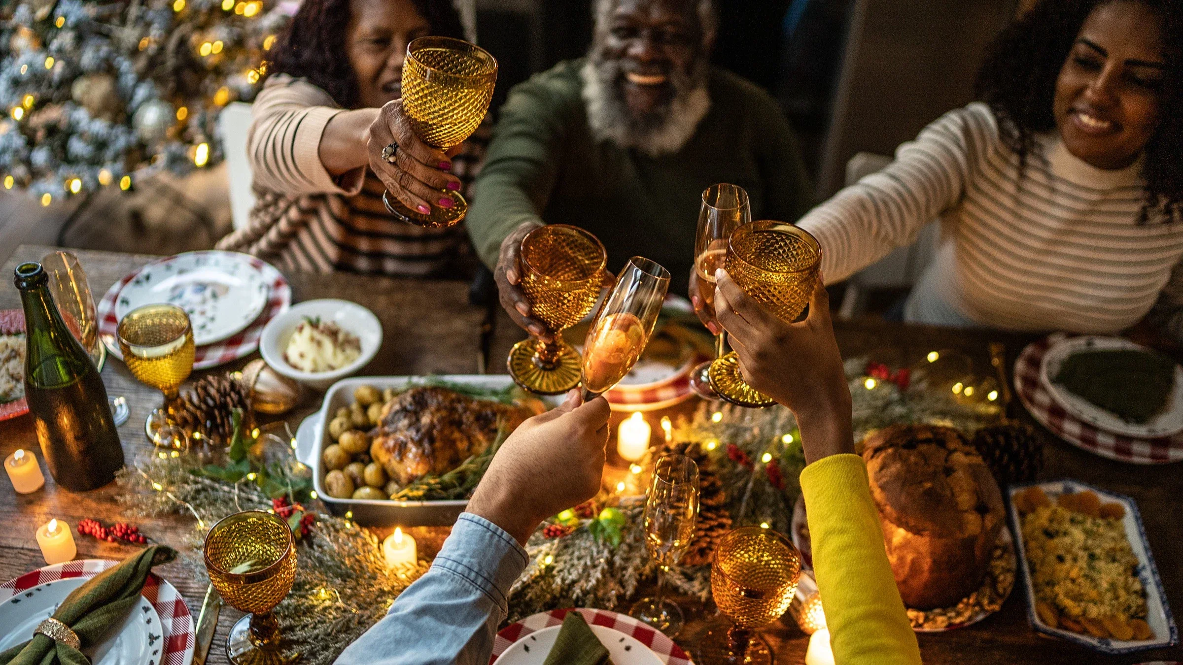 Family toasting at their Christmas dinner. There is a beautifully decorated table center with chicken and potatoes, bread, and stuffing.
FG Trade/E+ via Getty Images