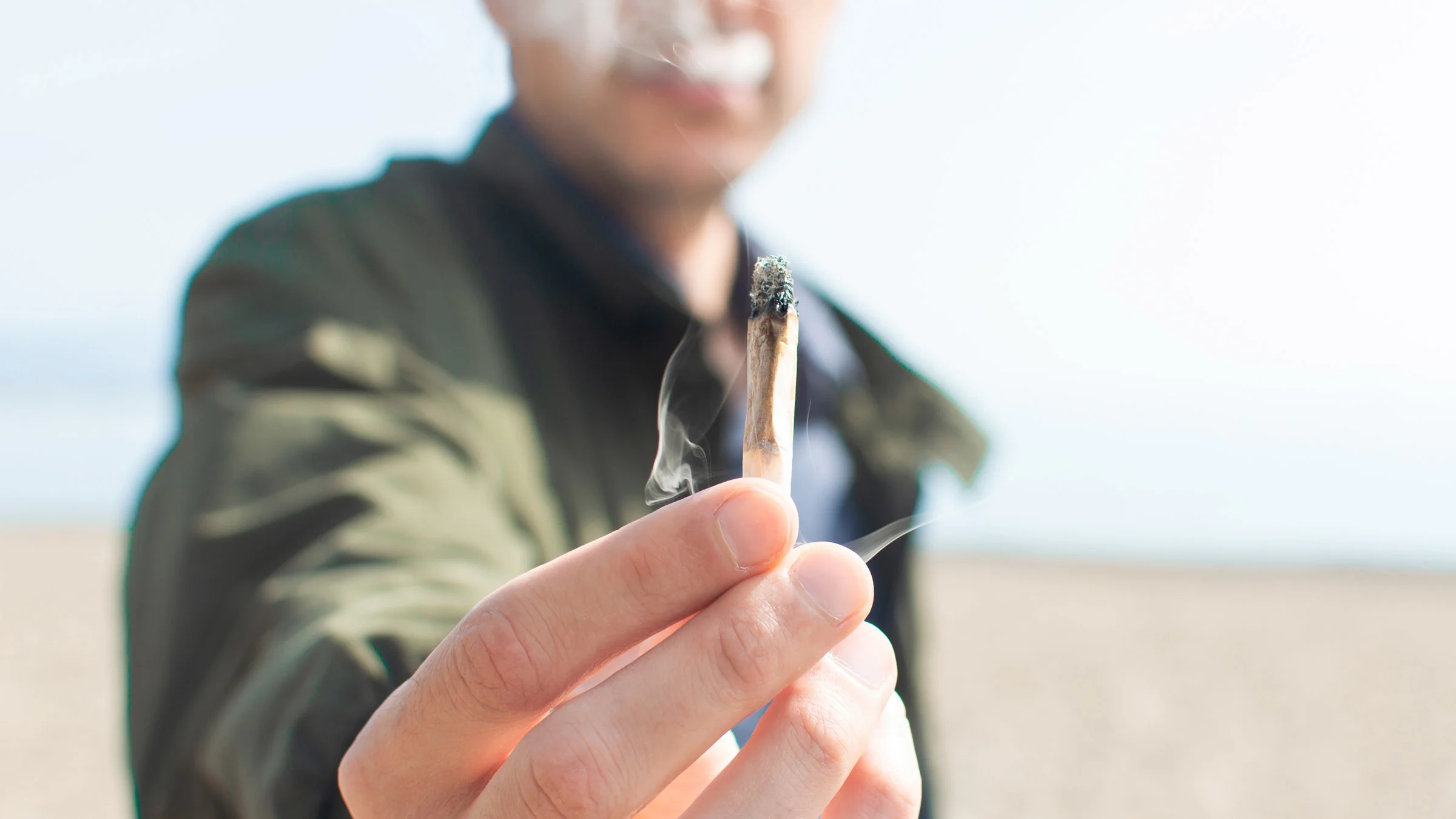 A cropped shot of someone passing a joint on the beach.