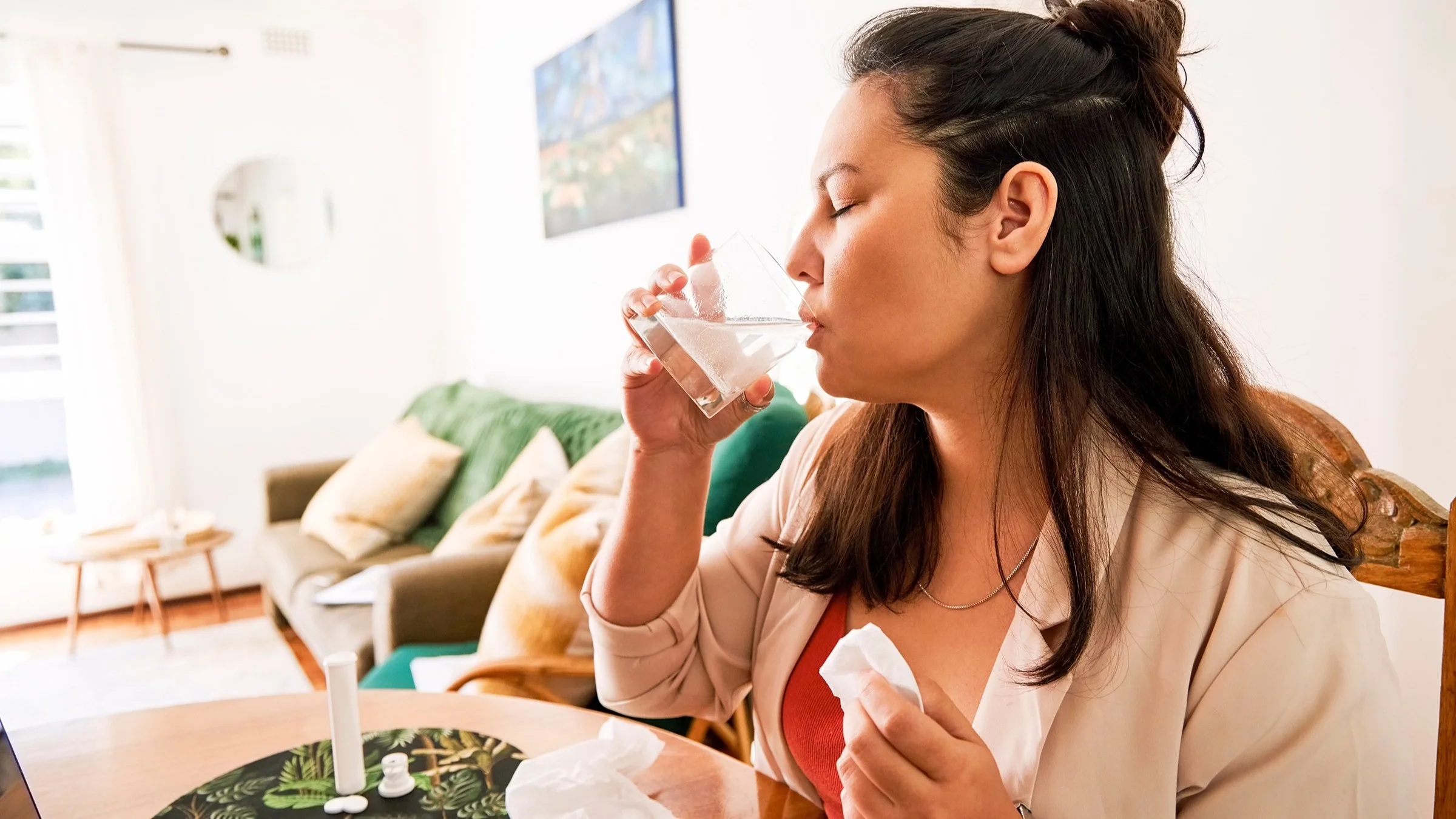 Woman with a half pony tail taking alka seltzer tablet in water. She has a tissue in her hand as well.