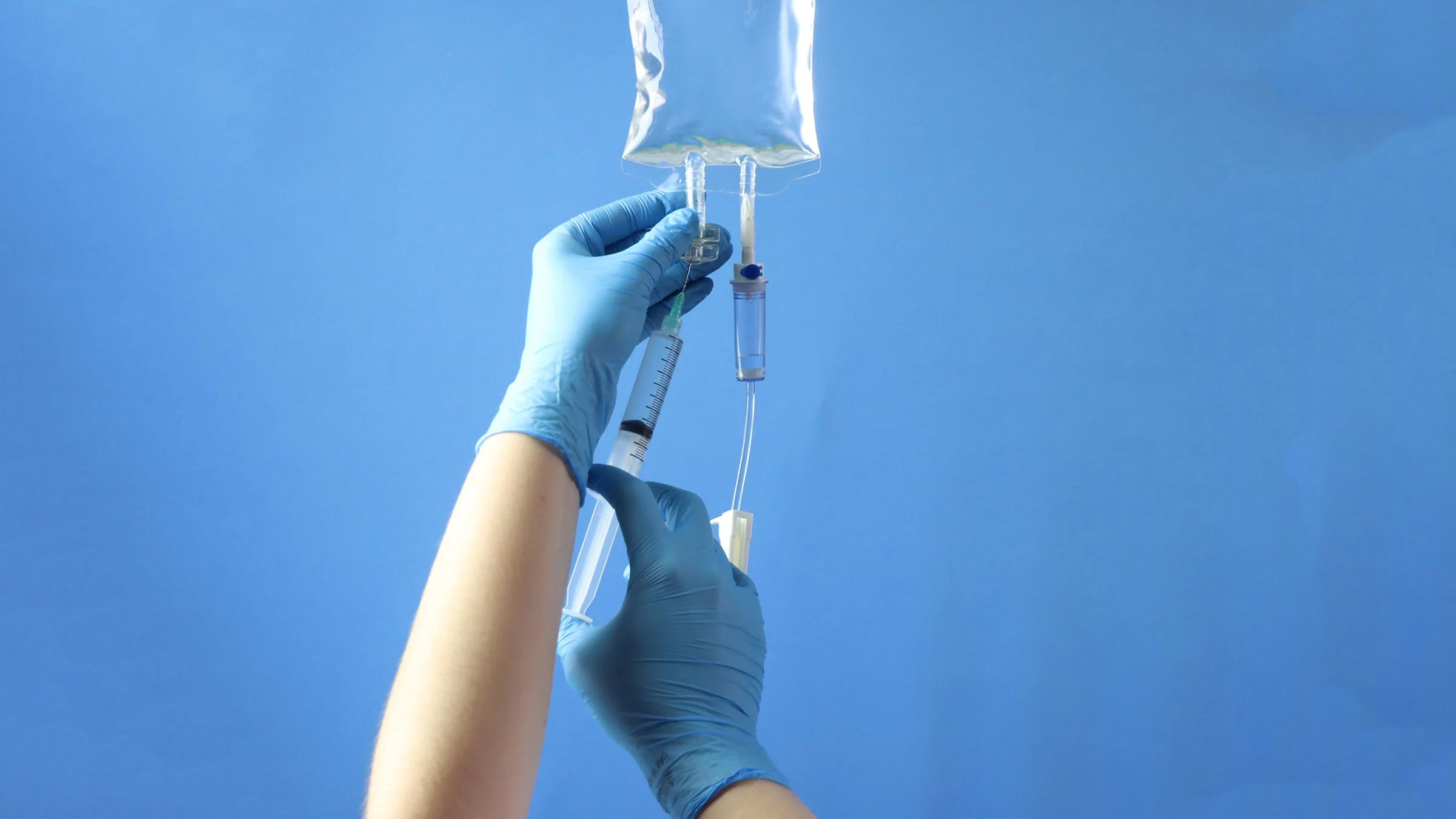 An IV bag with a syringe is shown in a close-up.