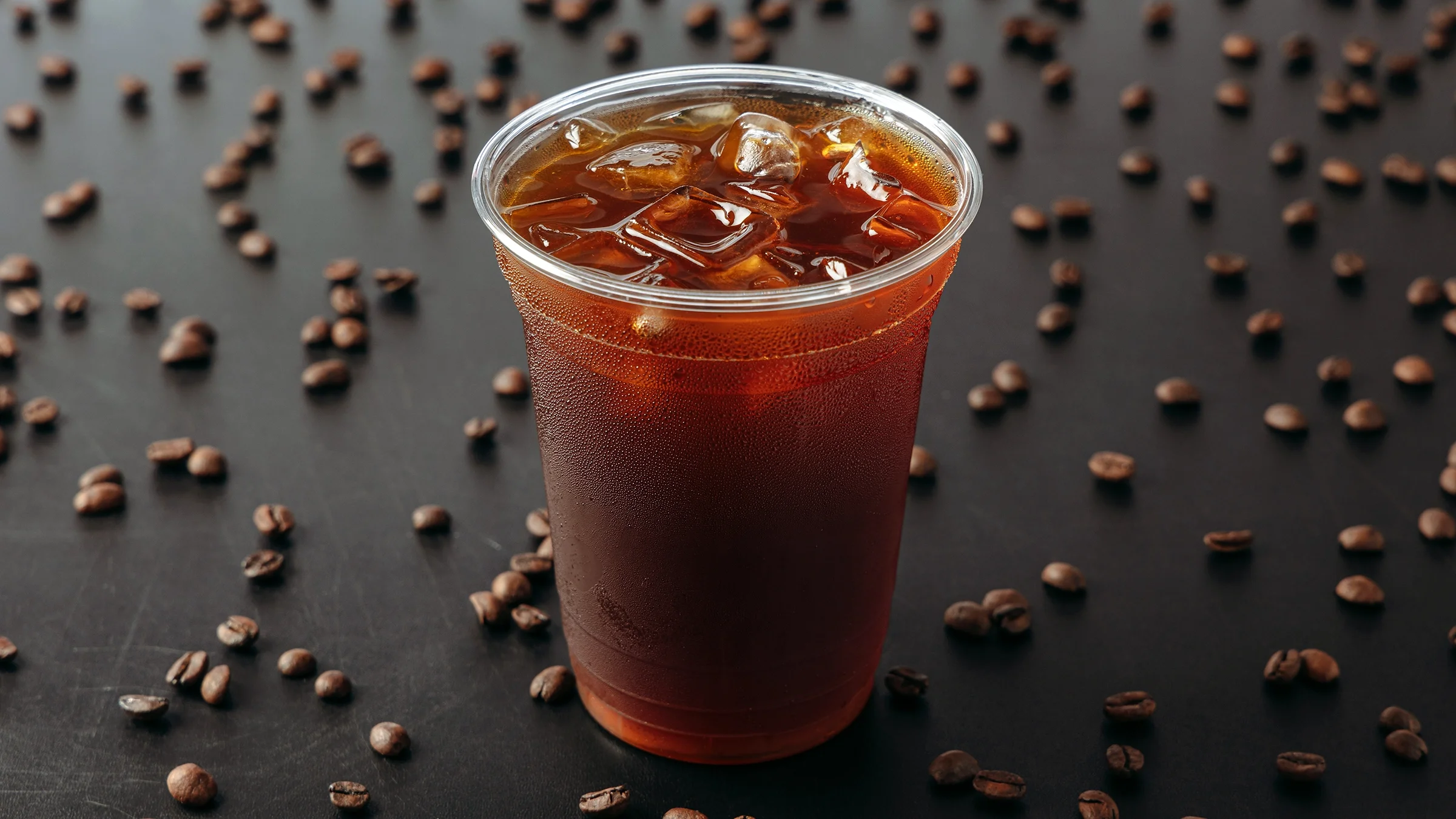 A cup of cold brew coffee stands on a black background with coffee beans.