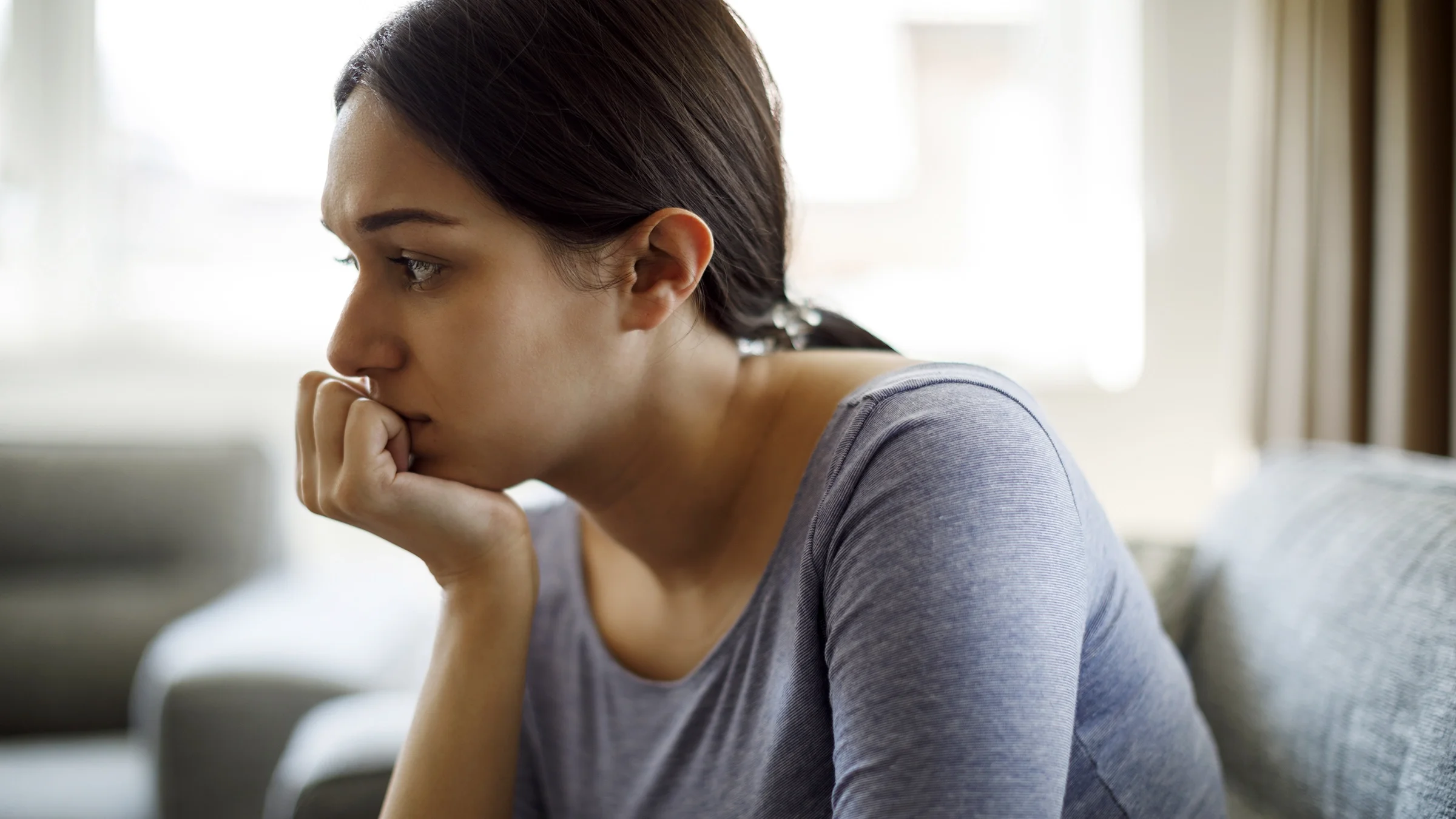 A visibly upset woman sits on a sofa alone at home.