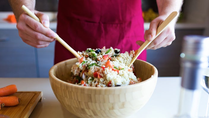 A cook prepares a bowl of quinoa salad.