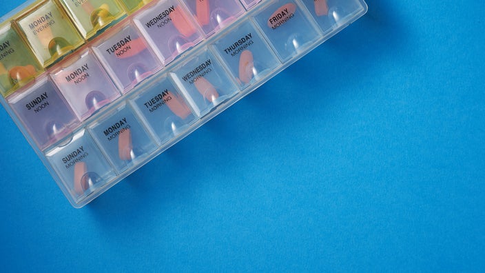 Cropped shot of a pill organizer on a blue background.
