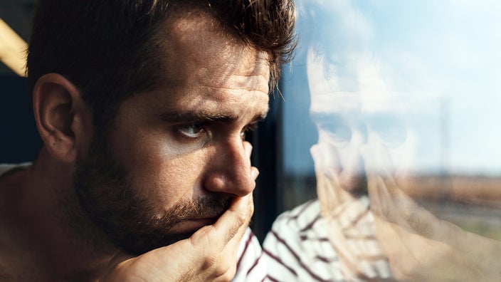 A man looks sad as he gazes through a window.